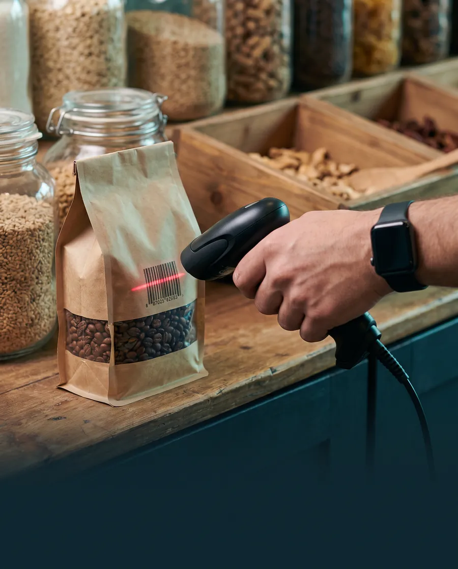 A hand scanning the barcode on a bag of coffee beans with a handheld scanner at a shop counter